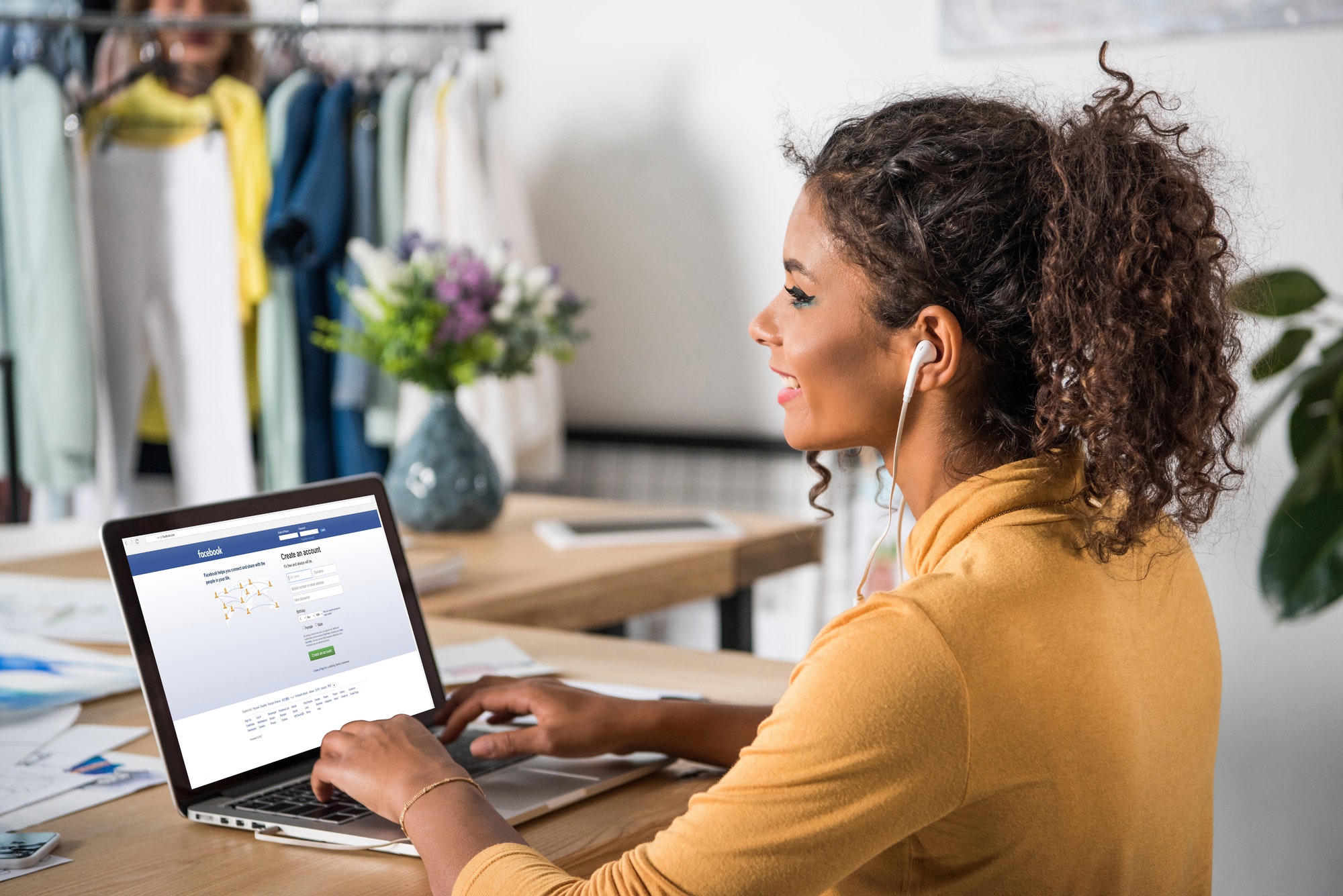 young happy african american woman in earphones using laptop with facebook website